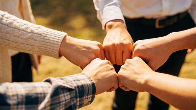 Four people joining hands in a circle outdoors, symbolizing unity and teamwork.