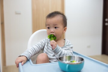 Baby eating broccoli sitting on high chair
