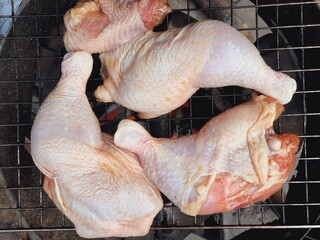 Grilling raw chicken legs over charcoal.