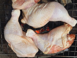 Grilling raw chicken legs over charcoal.