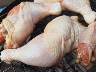 Grilling raw chicken legs over charcoal.