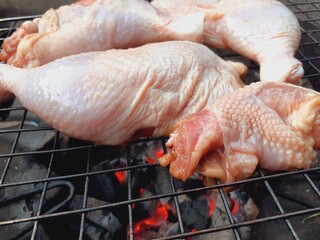 Grilling raw chicken legs over charcoal.