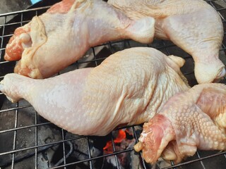 Grilling raw chicken legs over charcoal.