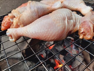Grilling raw chicken legs over charcoal.