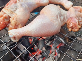Grilling raw chicken legs over charcoal.