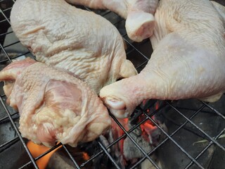 Grilling raw chicken legs over charcoal.