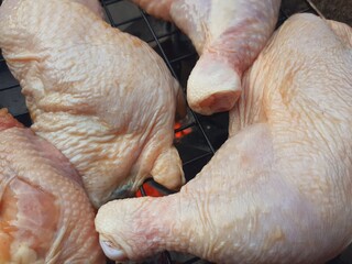Grilling raw chicken legs over charcoal.