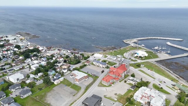 Aerial view of St Ann Catholic Church near Sainte Anne des Monts in Quebec town with houses and mountains. g.