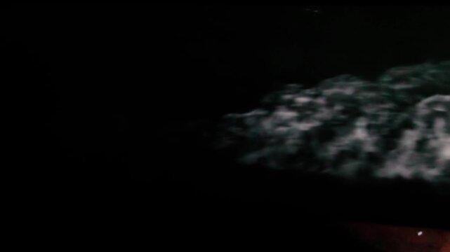 Cinematic footage captures a mesmerizing top-down perspective from the stern of a moving ship navigating a river at night. The video highlights the stark contrast between the deep black darkness