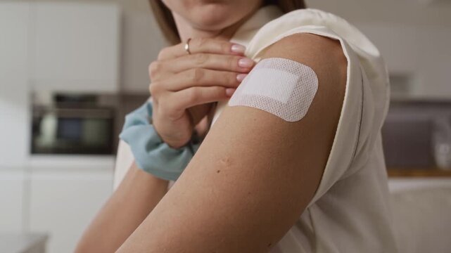 Closeup of young woman applying transdermal patch on her upper arm while getting ready in bright home setting as part of her morning wellness routine