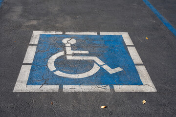 Cracked blue and white handicap parking symbol painted on asphalt pavement