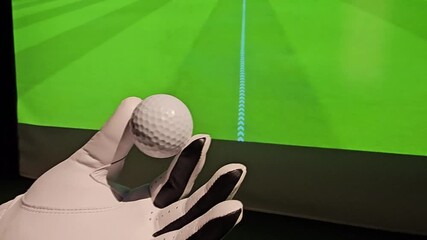 Golf ball held in hand before being putted on an indoor green in a golf simulation setup during a practice session - Powered by Adobe