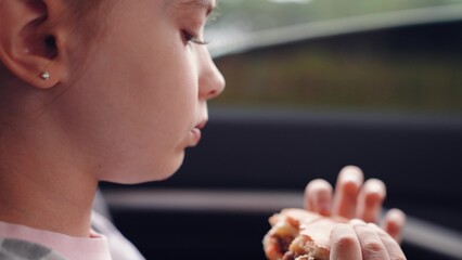 little girl child eating burger in car, happy person, girl enjoying burger car, Child eating cheeseburger during road trip, Little girl having snack back seat, Kid fast food on the go, Happy child