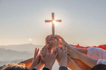 Silhouette family hands praying and holding Christian cross for worshipping God on mountain at sunrise background. Christian, Christianity, Religion copy space background. Easter Sunday concept:
