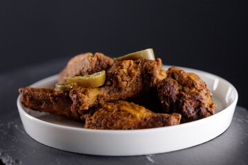 Crispy fried chicken wings with pickles on white plate against dark background