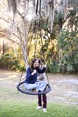 Young woman swings outdoors while man pushes her joyfully.