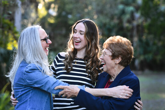 Three generations of women laughing and hugging outdoors.