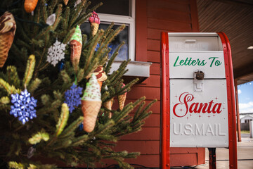 Santa mailbox beside a decorated Christmas tree with colorful ornaments in an outdoor holiday setting.