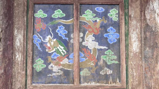 Ancient painted dragon on a wooden window shutter at Erdene Zuu Monastery, Mongolia. The traditional Buddhist art features a mythical creature and clouds on a weathered blue panel.