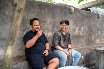 Two Asian Men Chatting Over Coffee at Outdoor Cafe in Indonesia