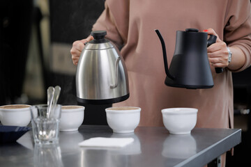 Female barista preparing coffee with kettles in factory setting