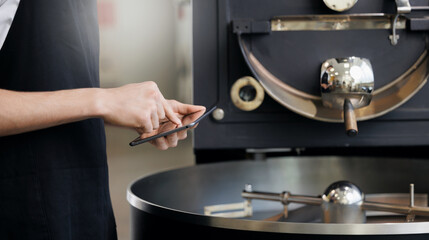 Male worker use tablet computer operating coffee roasting machine in industrial setting