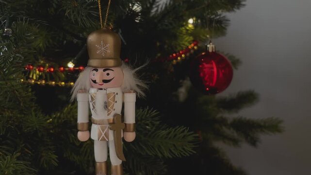 Large tin nutcracker soldier on a Christmas tree. Seasonal toy figure before an illuminated artificial Christmas tree with lights and colorful decorations. 