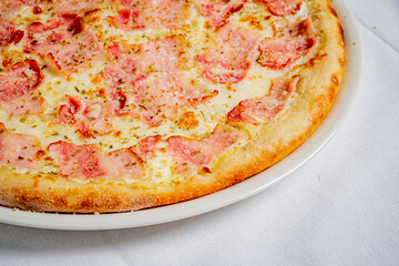 Tasty pizza has a golden crust topped with ham, cheese, and herbs, inviting everyone to enjoy