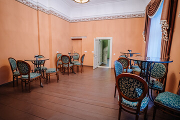 Elegant interior of a vintage cafe featuring ornate wooden tables and chairs with green upholstery, warm orange walls, and a doorway leading to another space, creating a cozy atmosphere