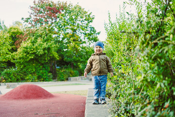 Smiling child explores vibrant playground path surrounded by lush greenery and autumn colors on a pleasant day