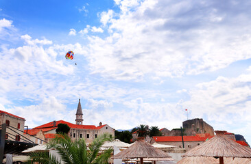Picturesque view of old town and tourists on a parachute, Budva, Montenegro. Topic of summer vacation, travel, leisure for adventure tourist. Popular tourist pastime with parascending
