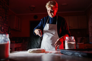 Elderly woman preparing dough in kitchen for baking