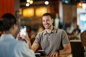 Woman photographing smiling man with phone in coffee shop