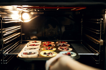 Baking berry muffins in hot oven with person's hand