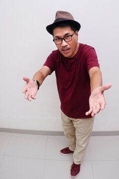 Man in his casual clothes and wearing a hat opening both arms to welcome people