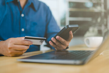 Customer verifying an online purchase with a credit card and smartphone at an office desk, representing secure mobile payments, e-commerce banking, and convenient digital transactions.