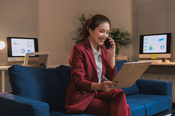 Asian businesswoman talking on phone holding clipboard in office