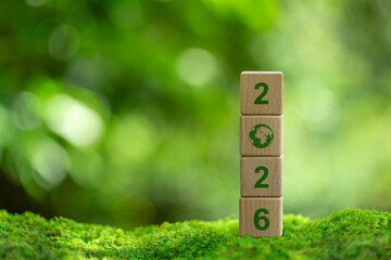 Wooden blocks with number 2026 and earth icon on green moss background for sustainable development,...