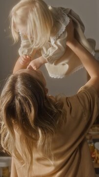 Vertical back view shot of happy caring mom playing with adorable little girl and holding her up in air with child laughing
