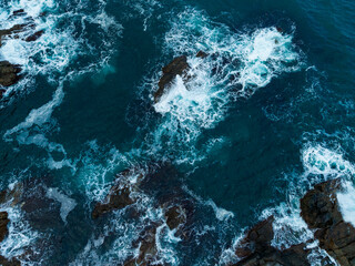 Waves crash against rugged rocks in a vibrant blue ocean under soft sunlight during midday in a coastal paradise