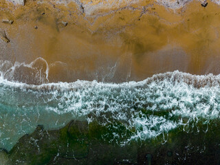 Breathtaking aerial view of golden beach and crashing waves under clear blue skies during a sunny day