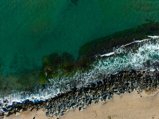 Waves crash against rocky shoreline during golden hour at a serene beach