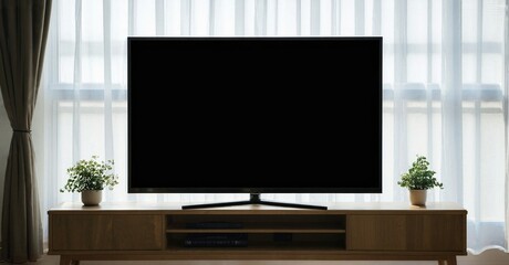 Fototapeta premium Living room interior features television set atop wooden console. Plants flank display, window provides soft light. Minimalist design.