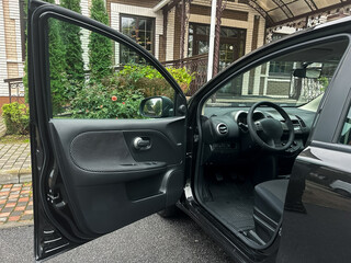 Black car parked near a cozy house with open door inviting exploration on a calm day filled with greenery and soft sunlight