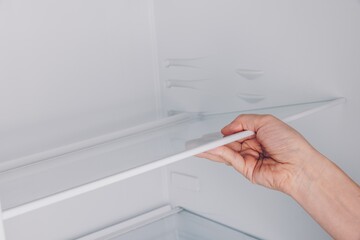 A Hand Adjusting a Shelf Inside a Clean and Empty Refrigerator, Highlighting Organization and Accessibility for Food Storage