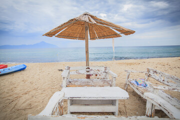 Rustic white benches under a straw umbrella on a Greek beach