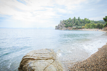 Large  boulder with waves in calm, light blue sea at overcast coast © mitarart