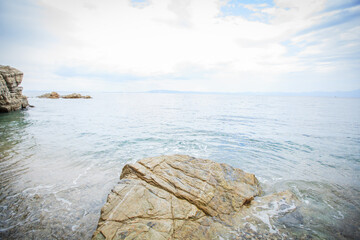 Large  boulder with waves in calm, light blue sea at overcast coast © mitarart