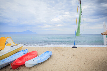 Obraz premium Colorful kayaks and pedal boat resting on sandy beach with distant mountains