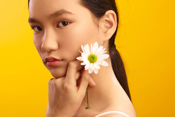 Asian woman stands against a vibrant backdrop with a flower, presenting a calm and graceful...